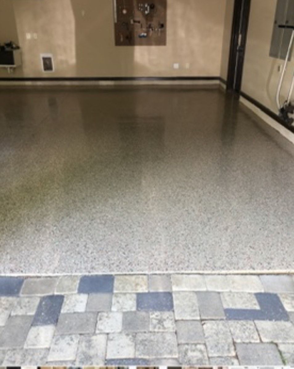 Garage with epoxy flooring, viewed from a paver patio. Gray and beige tones dominate.