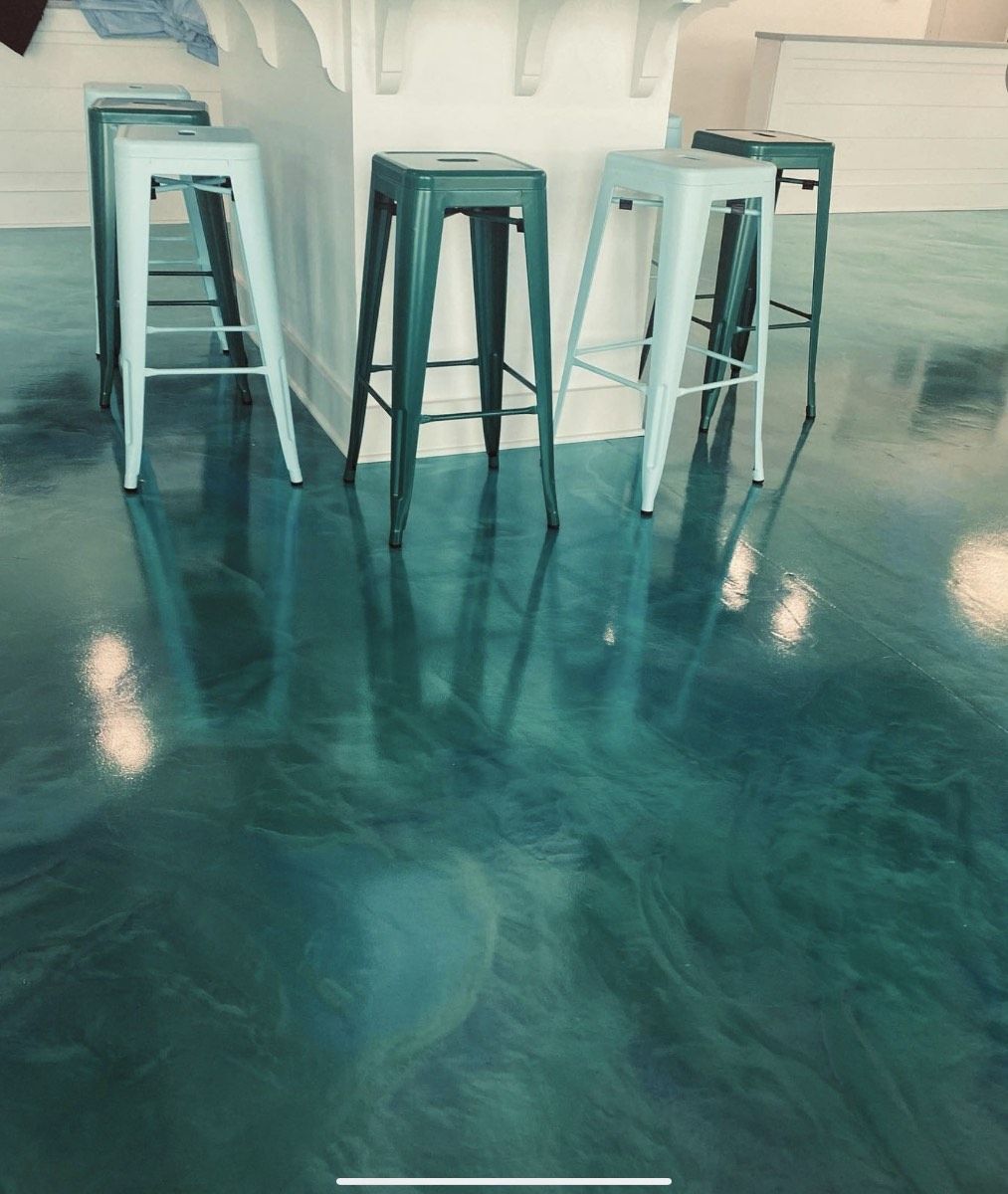 Shiny teal epoxy floor with metal bar stools in front of a white counter.