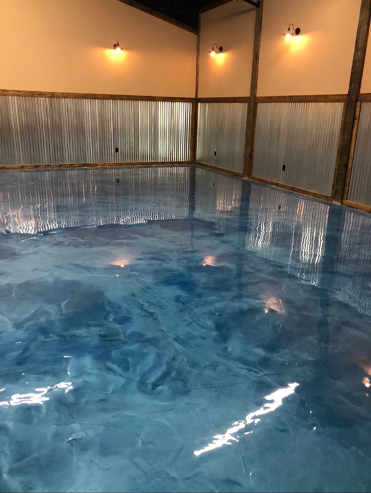 Blue epoxy flooring in a room with corrugated plastic walls, lit by overhead lights.