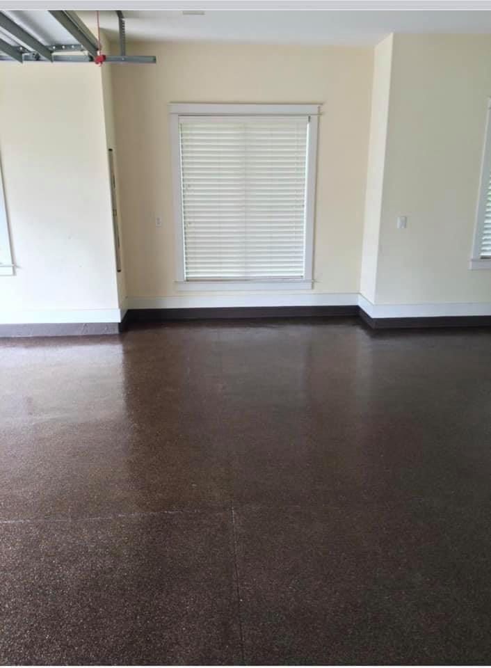 Empty garage with brown floor, cream walls, and window with blinds.