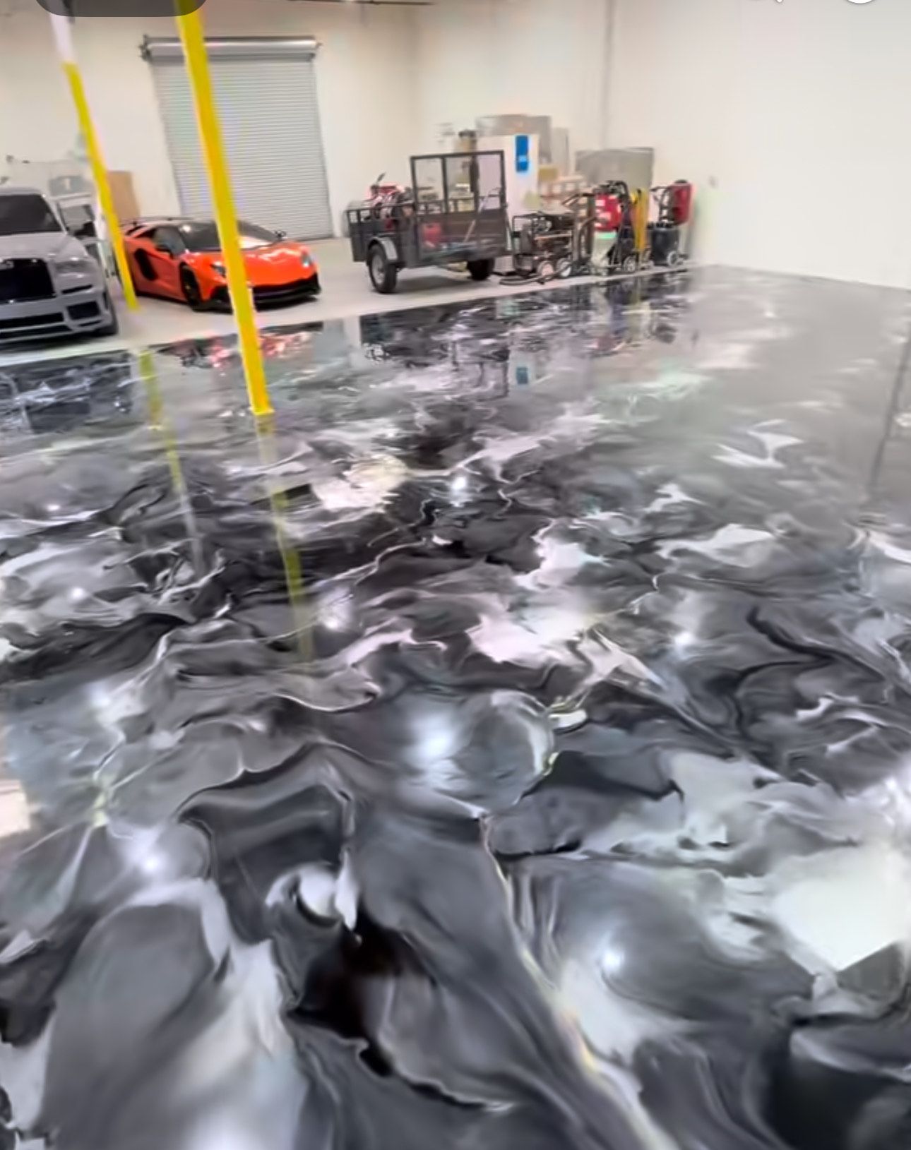 Epoxy garage floor with black, white, and gray swirls, reflecting vehicles and equipment.