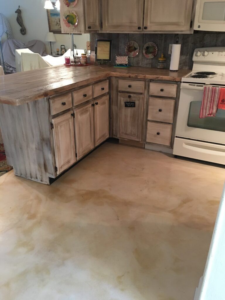 Kitchen with light-colored, distressed cabinets and countertops; stained concrete floor; white appliances.