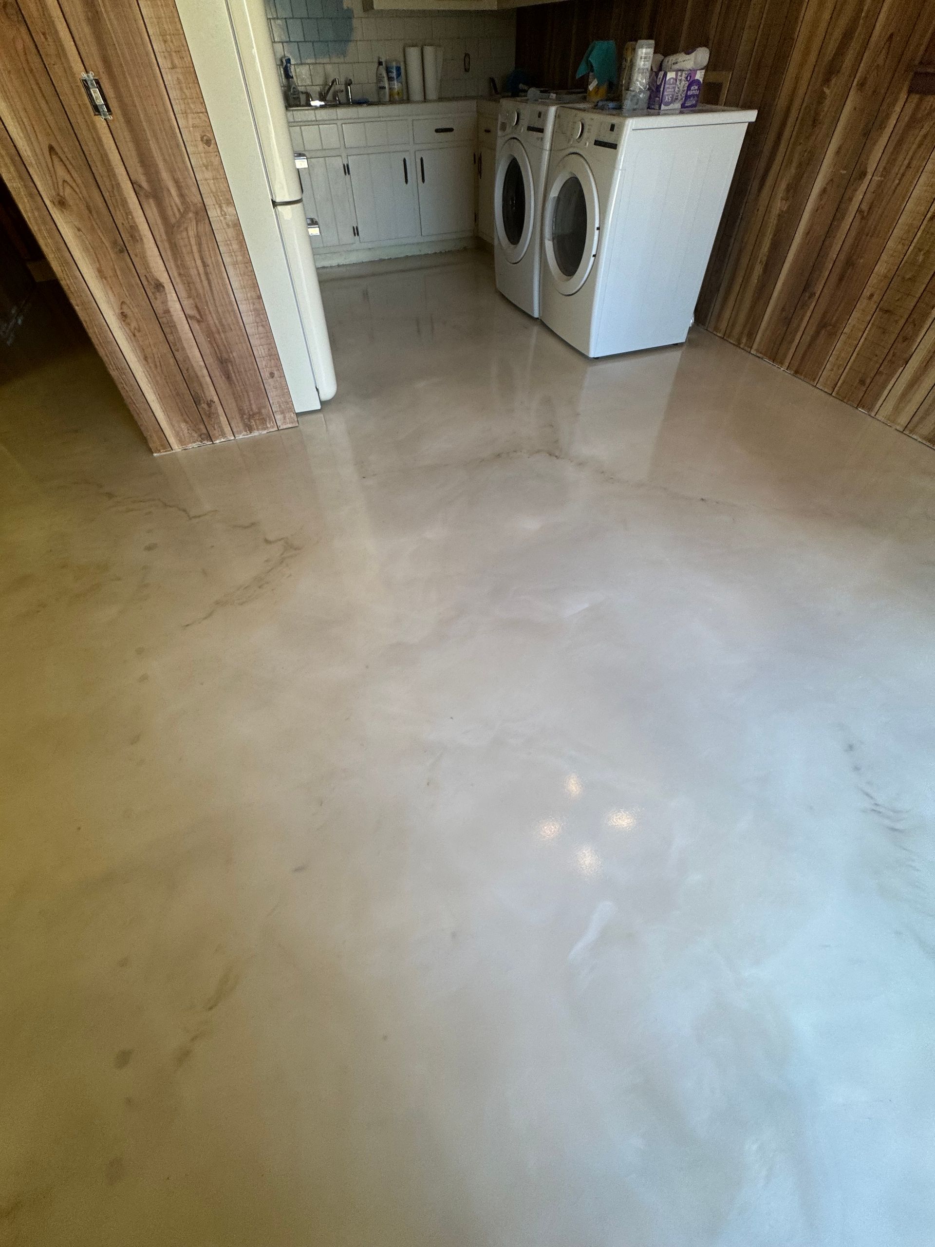Laundry room with polished, light-colored concrete floor, white appliances, and wood-paneled walls.