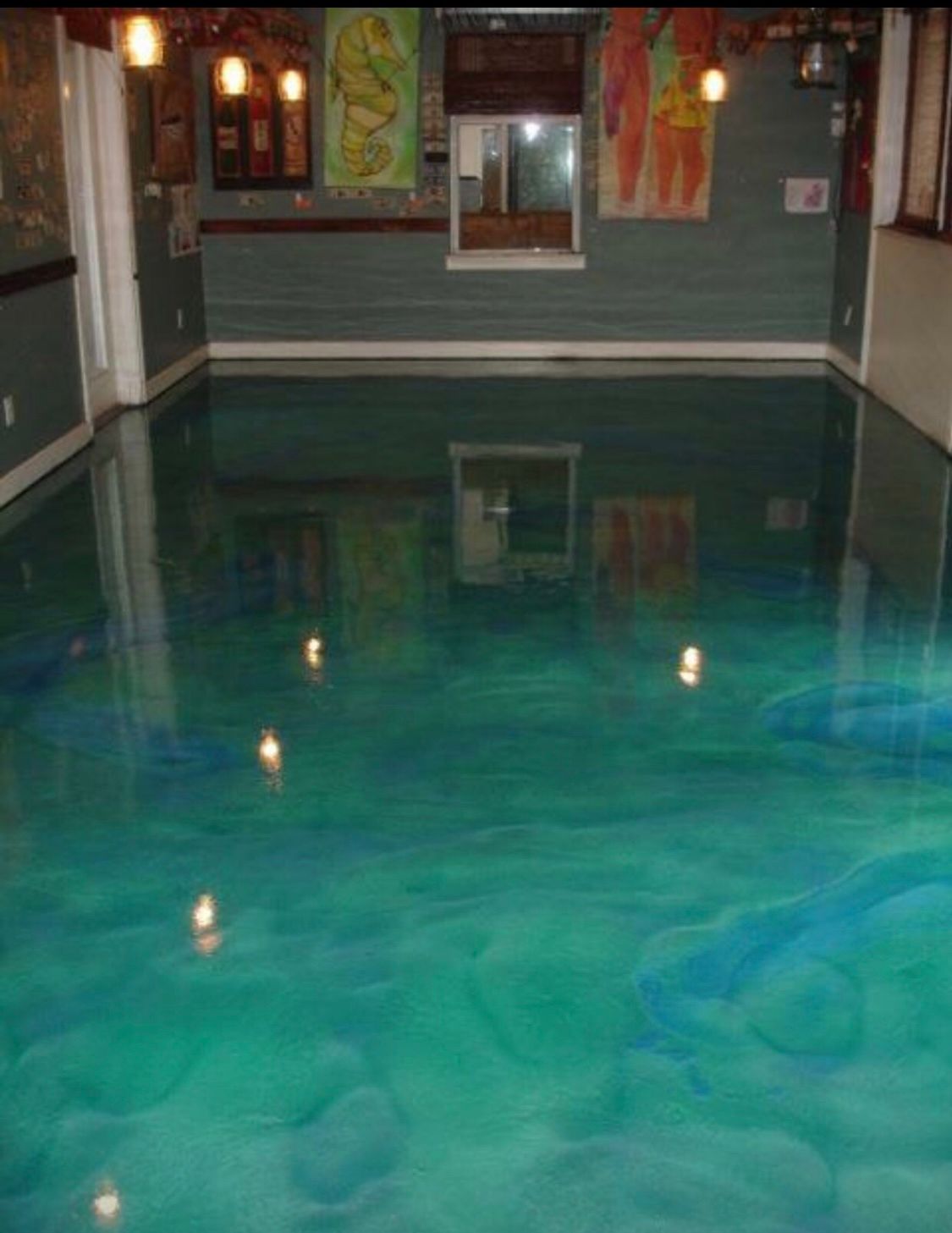 Epoxy floor with blue-green swirls. Reflective surface in a room with a bar and colorful art.