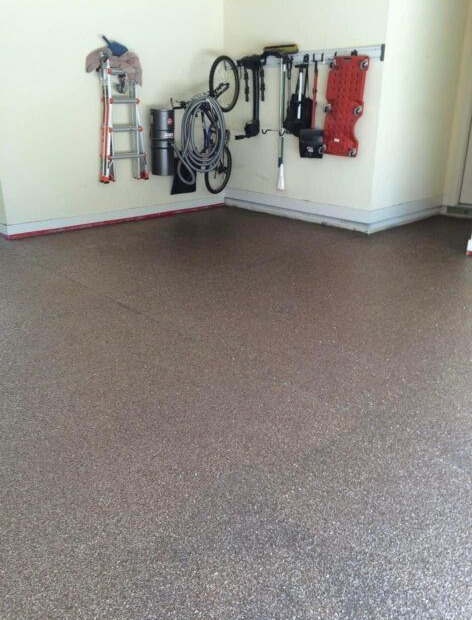 Garage interior with tools and a bicycle hanging on the wall. Speckled floor, beige walls.