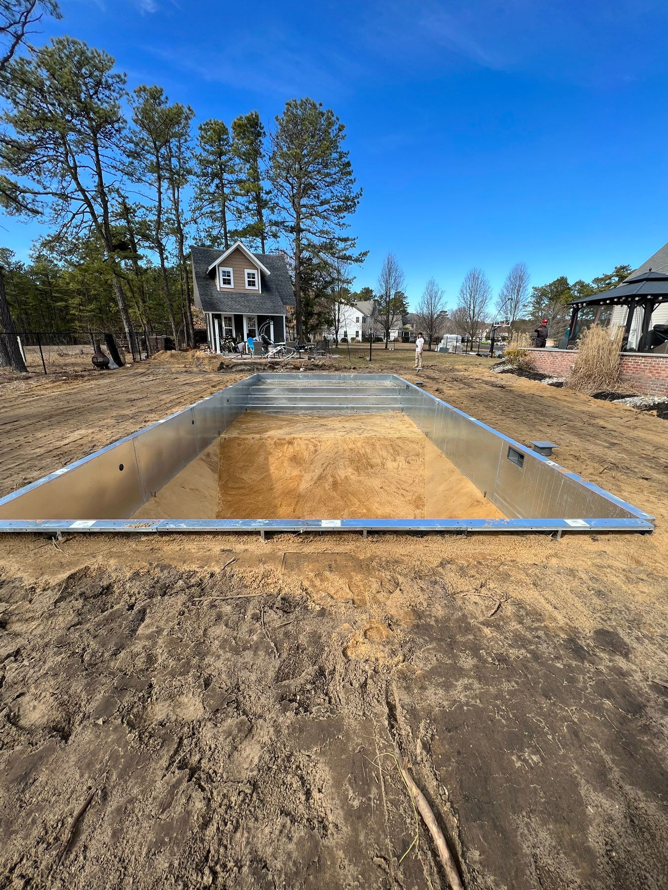 A swimming pool is being built in a dirt field in front of a house.