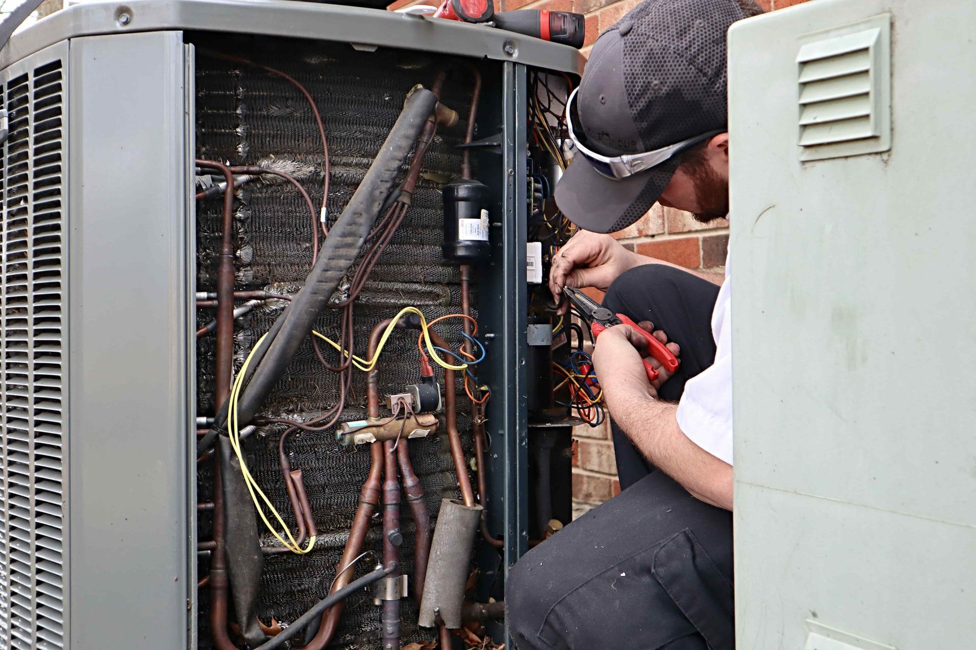 A man is working on an air conditioner with a pair of pliers.