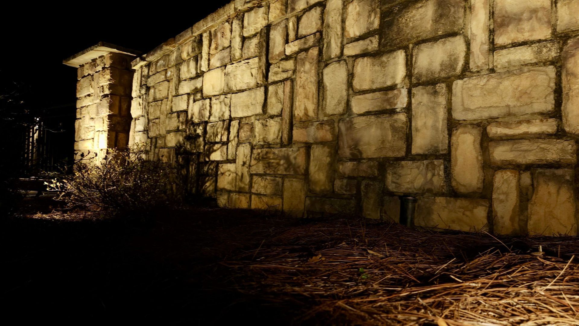 Warm uplighting showcasing stone wall textures in landscape design