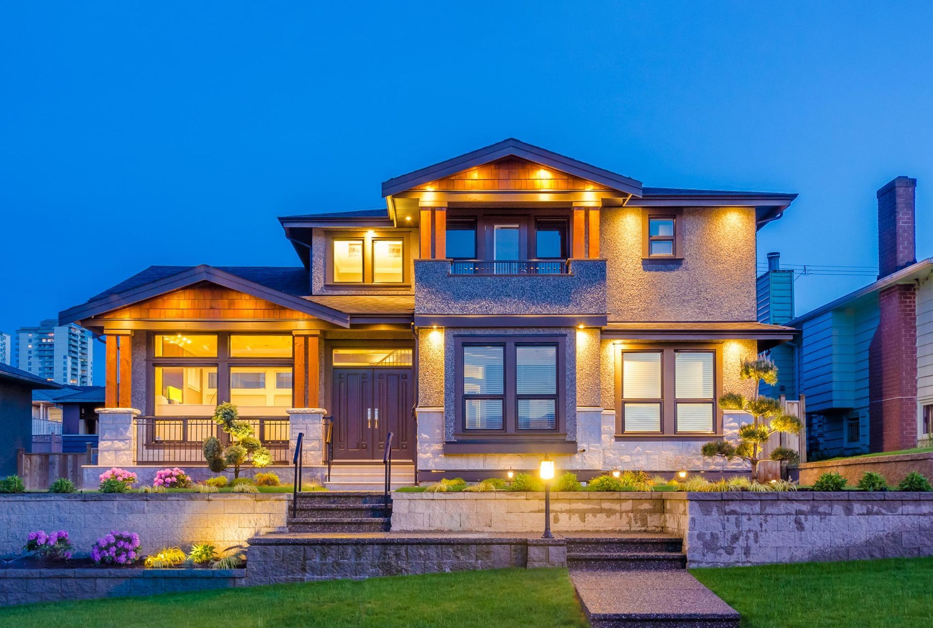 Modern two-story home with warm architectural lighting highlighting entryway and landscaping at dusk
