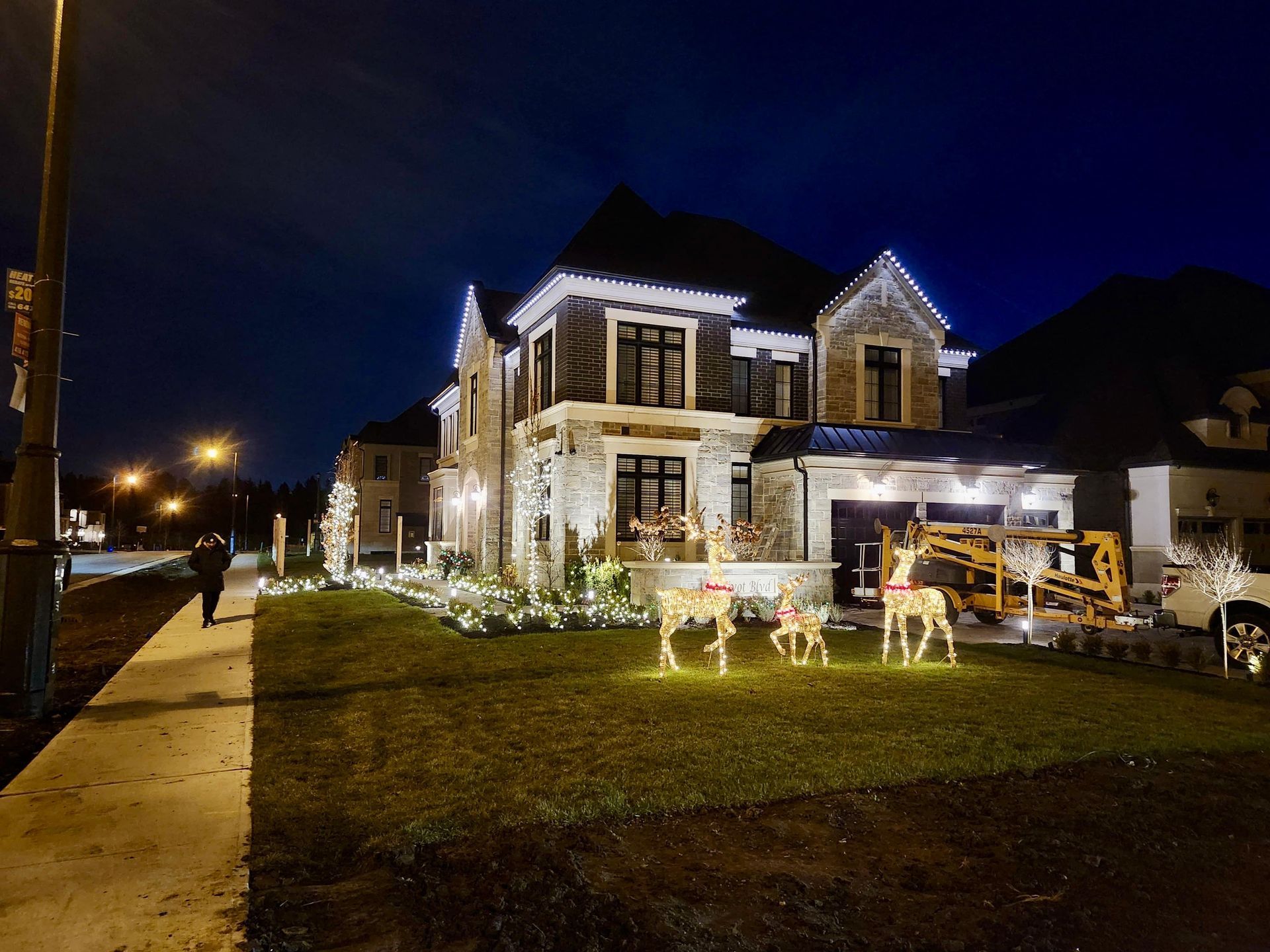 Suburban home with white permanent holiday lighting and LED reindeer decorations on front lawn