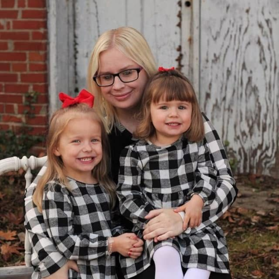 A woman in a blue shirt is taking a selfie in front of an alphabet poster.
