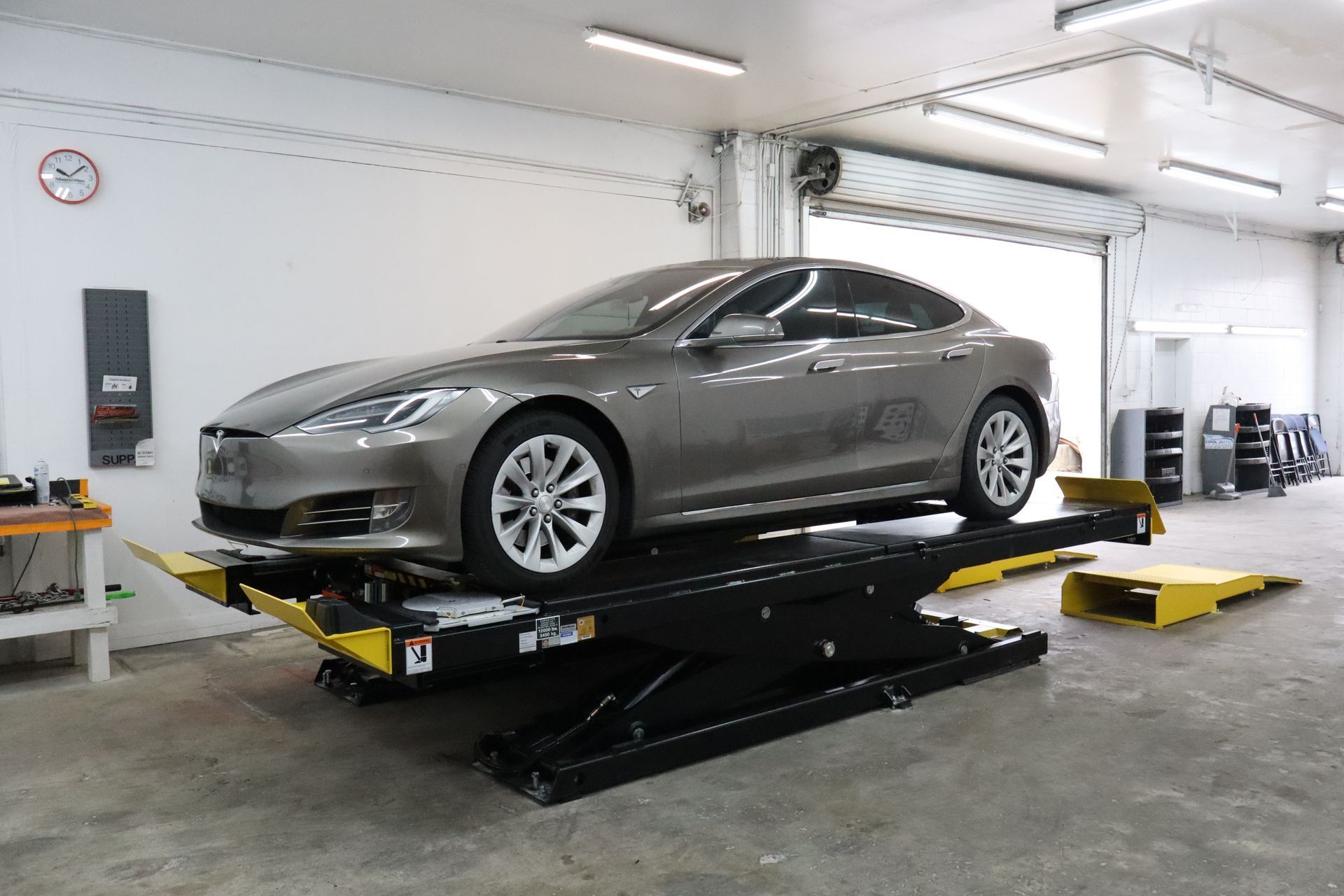 A tesla model s is sitting on a lift in a garage.