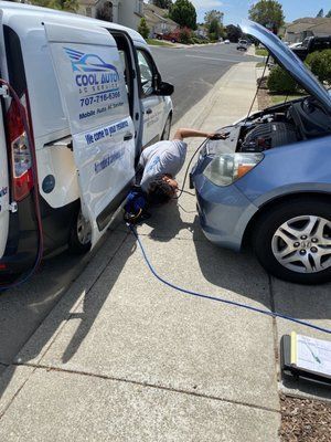 A man is working on a car on the sidewalk next to a van.