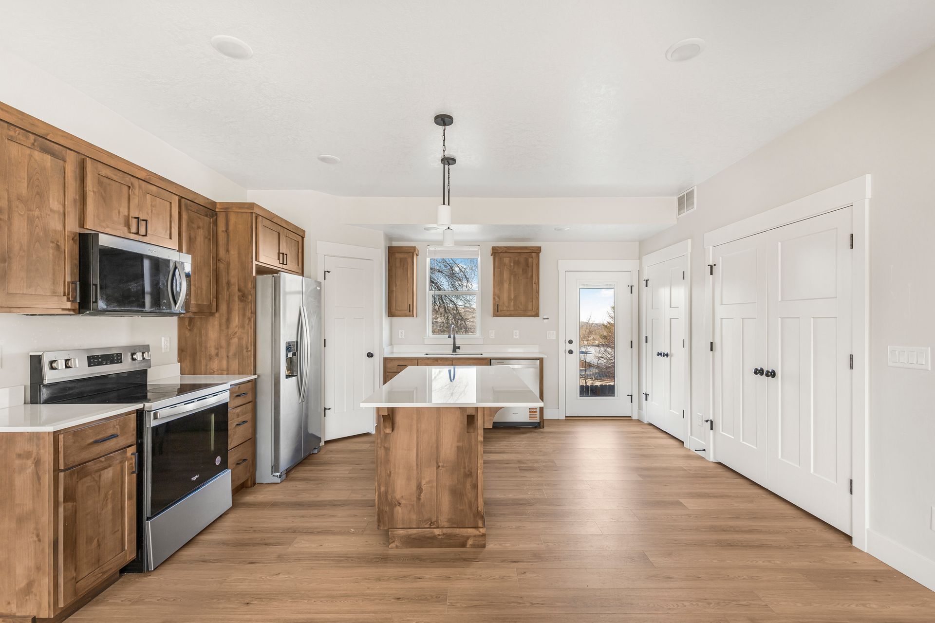 Wooden-cabinet kitchen with stainless appliances, island, and wood floors. Sunlight streams through a back door and window.