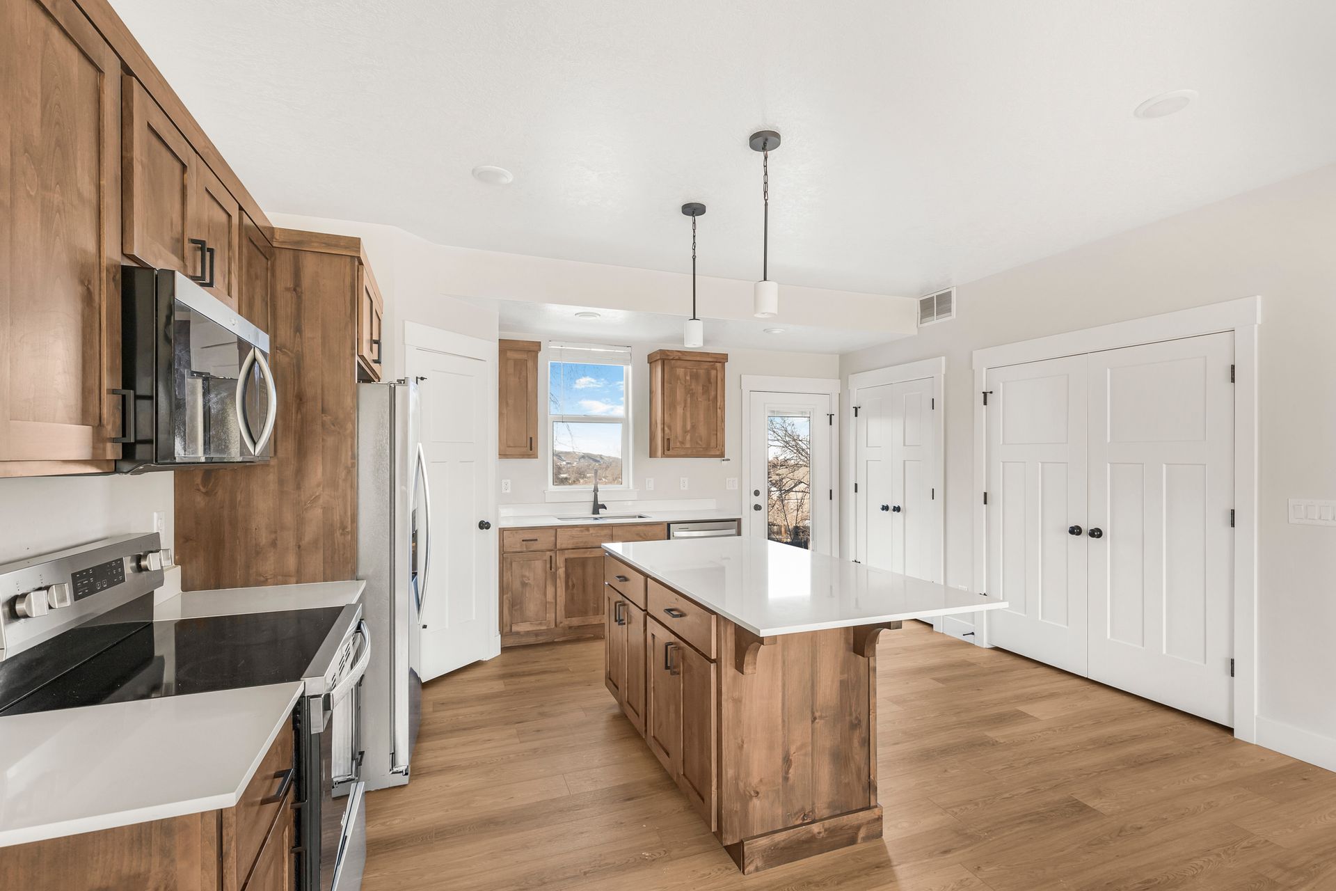 Kitchen with wood cabinets, white island, stainless steel appliances, and wood flooring.