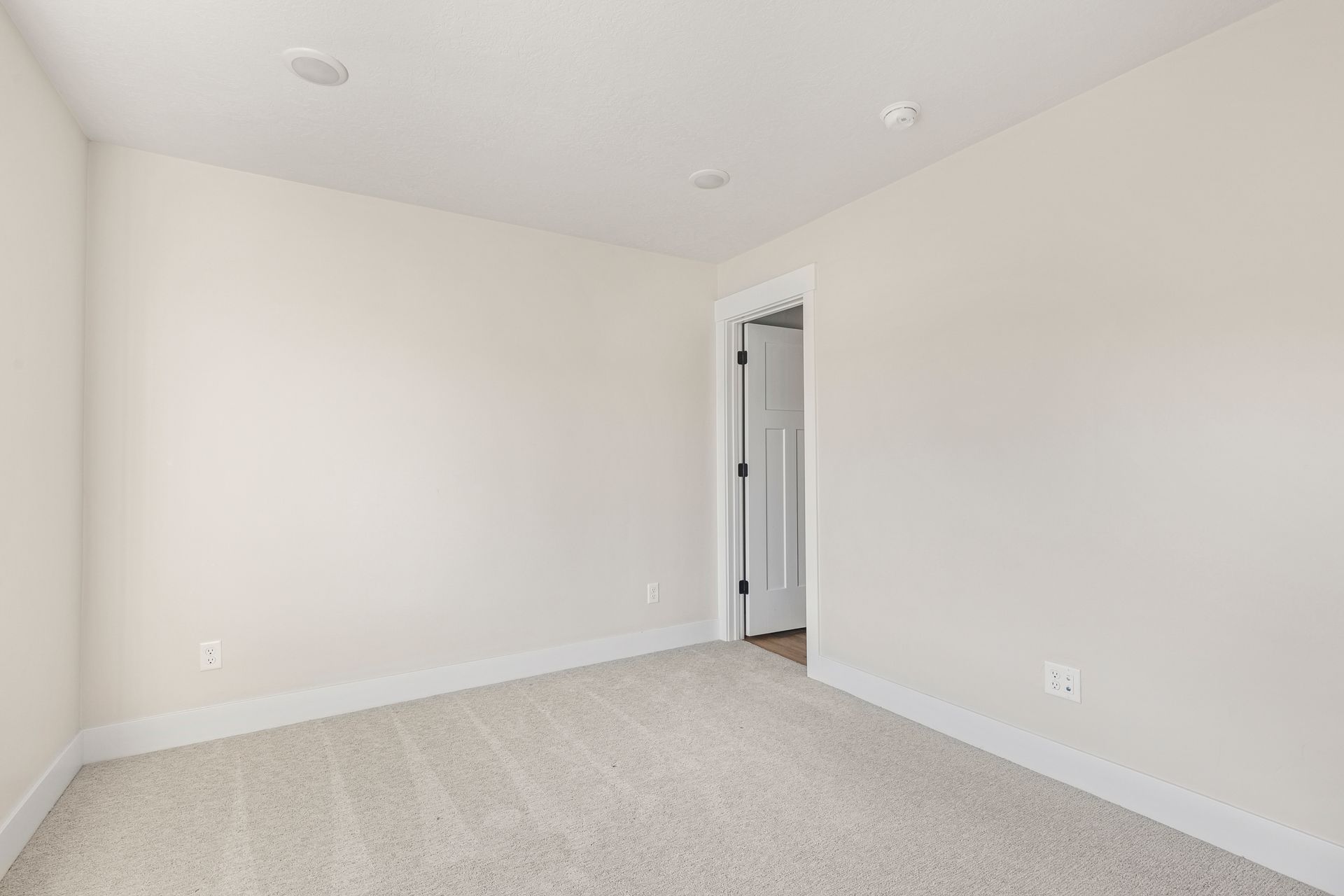 Empty room with beige carpet, white walls, door, and recessed lighting.