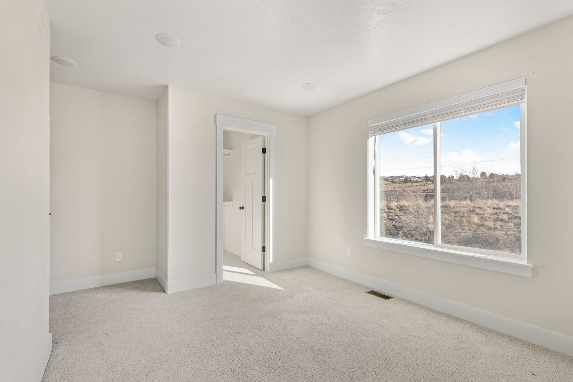 Empty bedroom with off-white walls, carpet, and trim, window with a view, and a partially open door to a closet.