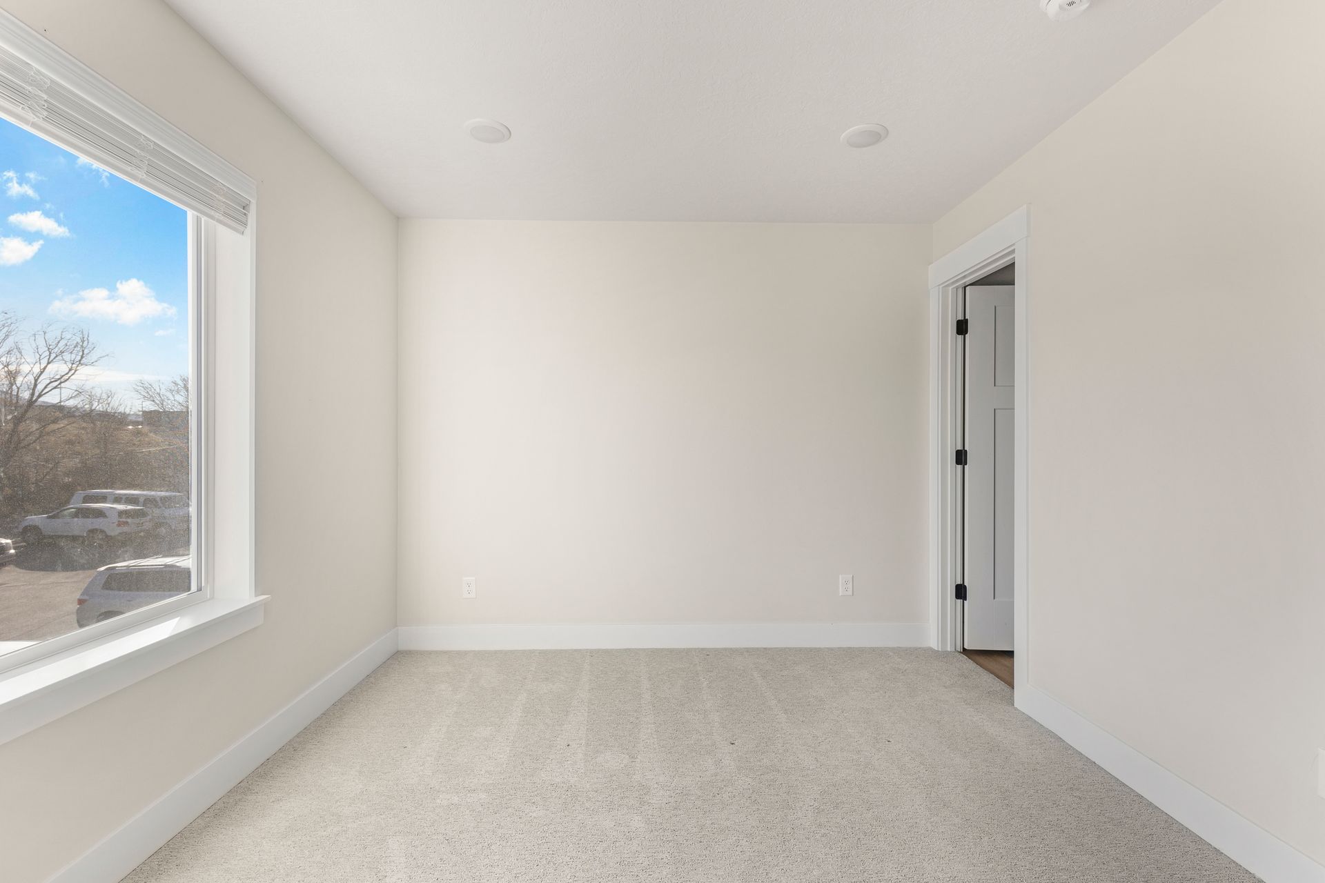 Empty room with a window, white walls, carpeted floor, and doorway.