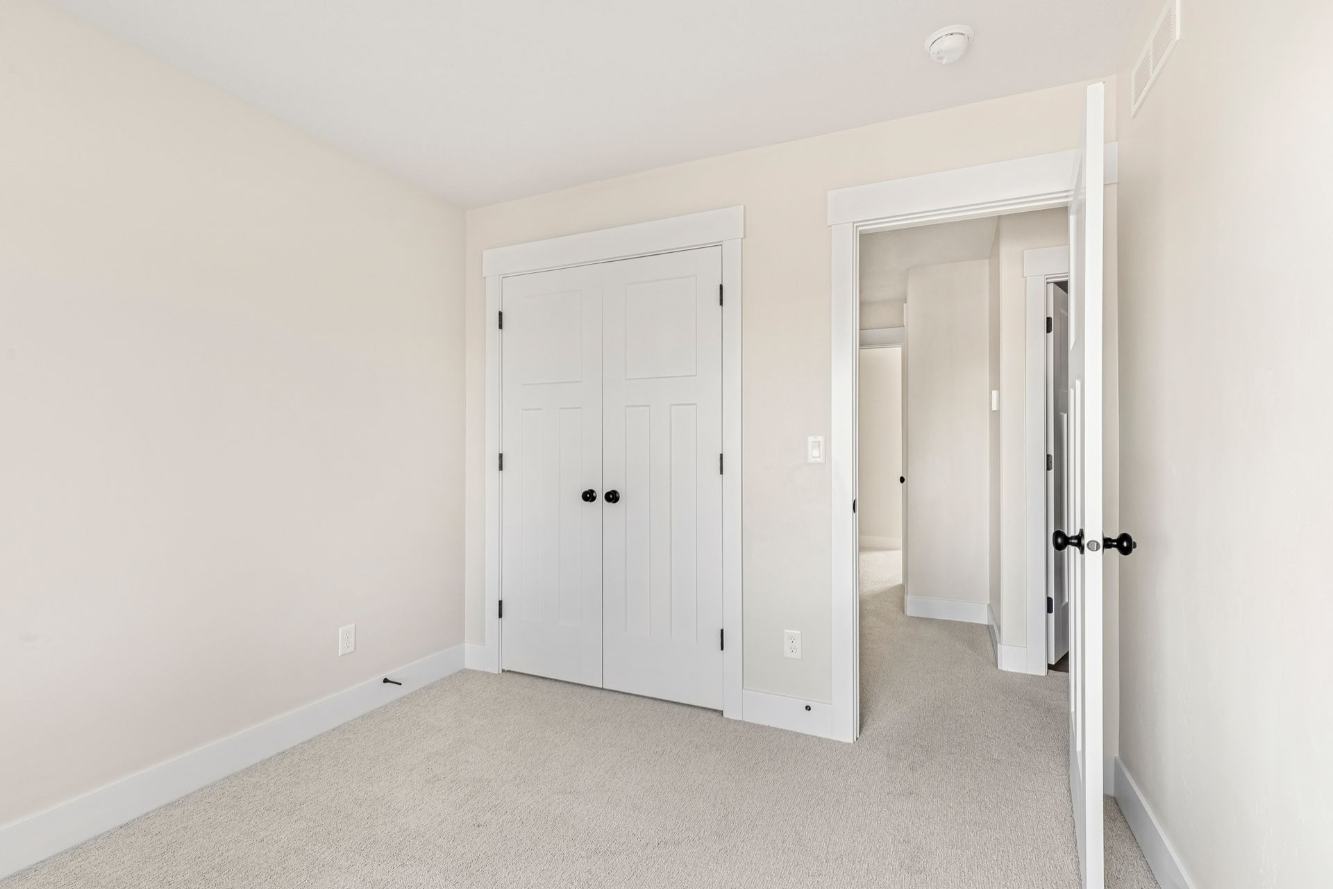 Empty bedroom with white walls, closet, and doorway to a hallway, light carpet.