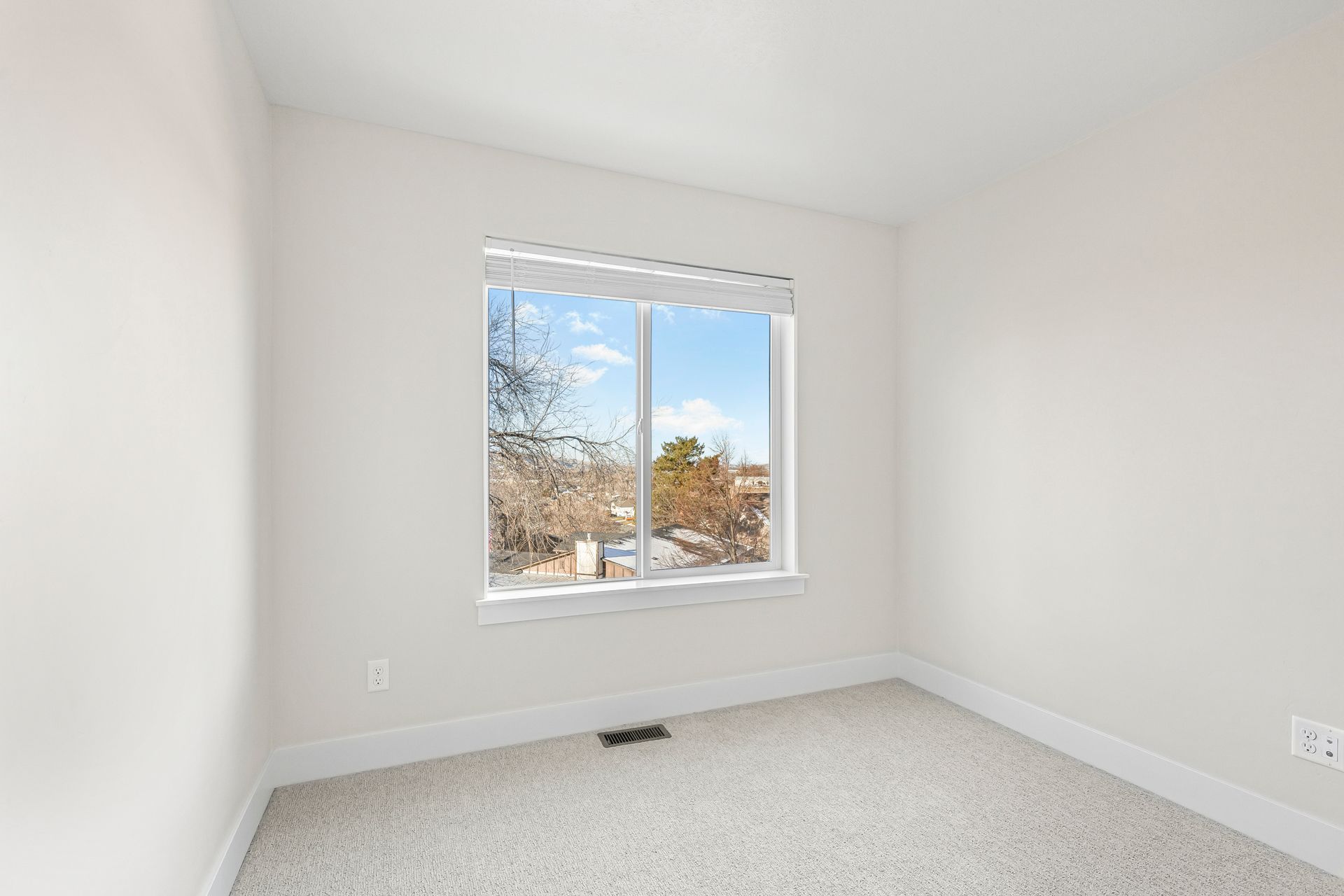 Empty room with white walls, carpet, window, and view of trees and sky.