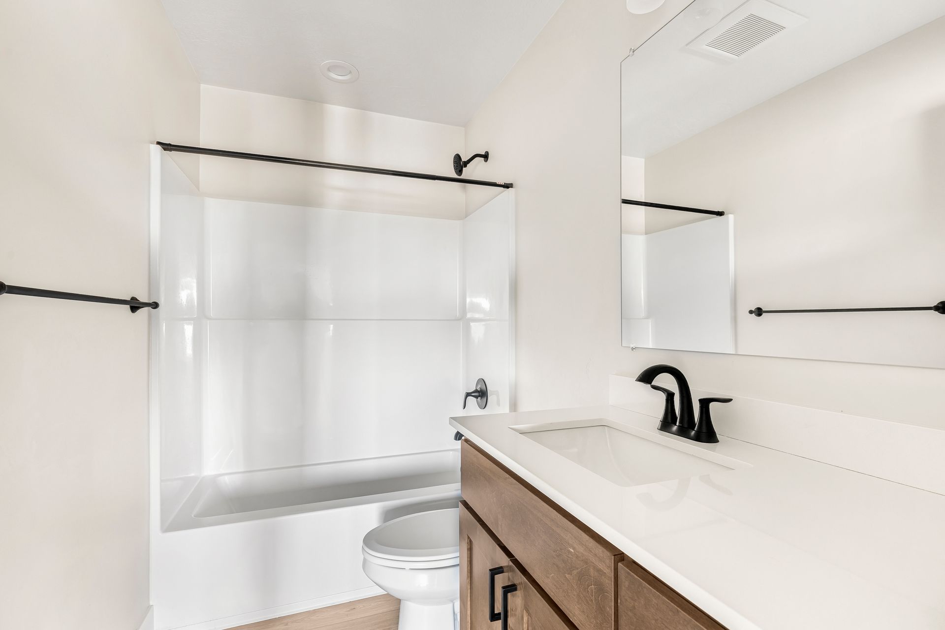 Bathroom with a white tub and walls, dark fixtures, and a wooden vanity.
