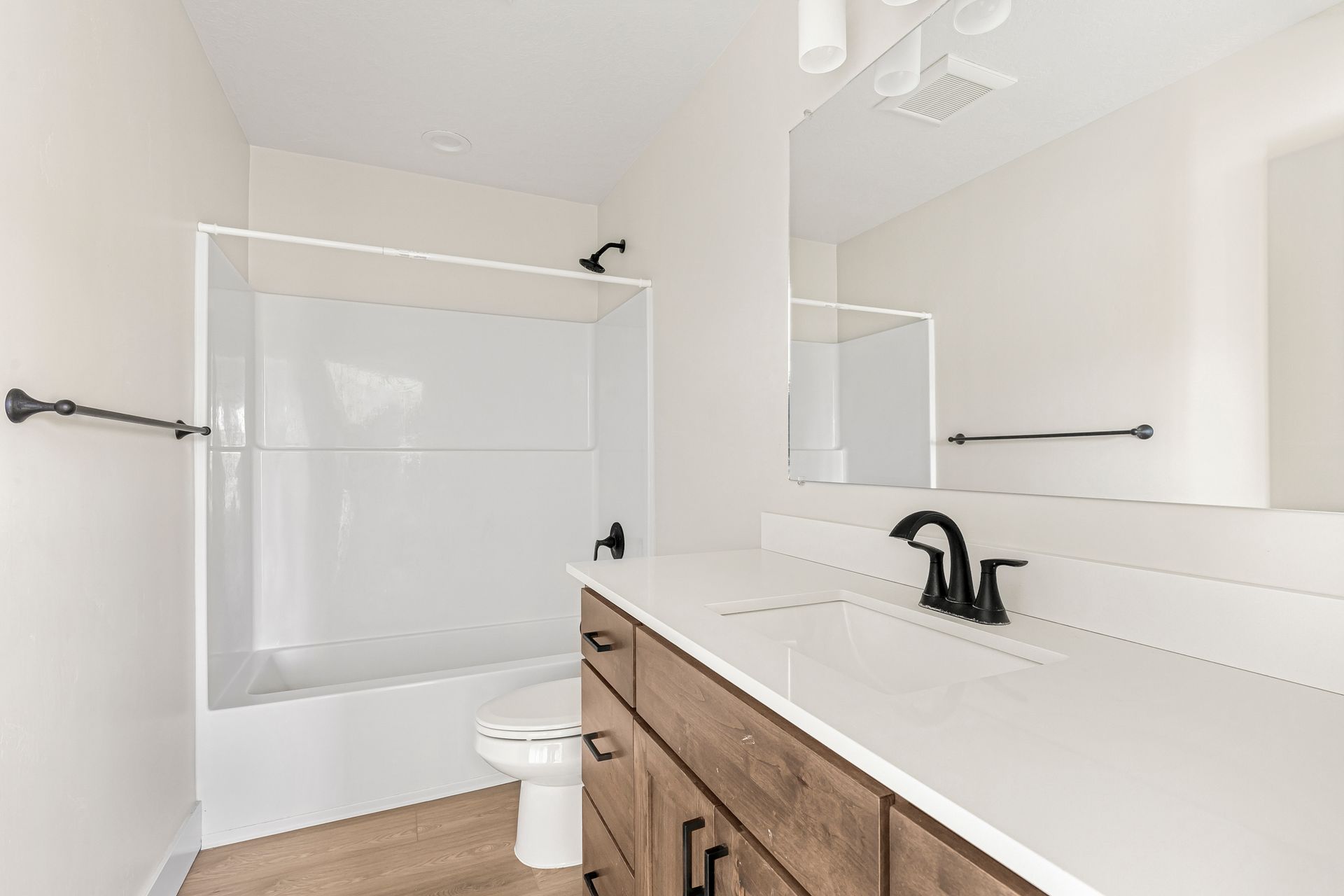 Bathroom with white tub/shower, vanity, and toilet; brown cabinet, black fixtures.