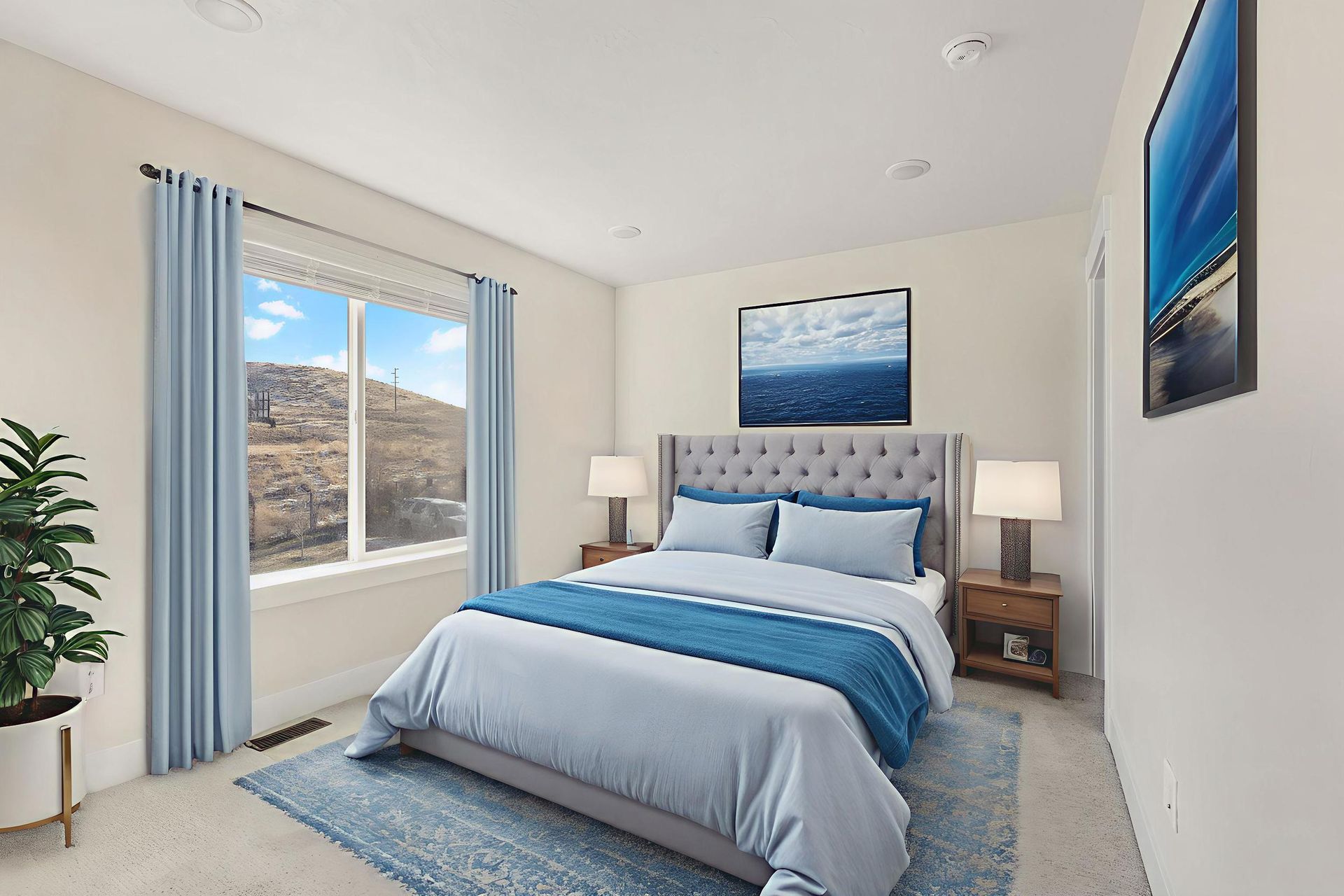 Bedroom with blue and white bedding, curtains, and rug, with art and wooden nightstands.
