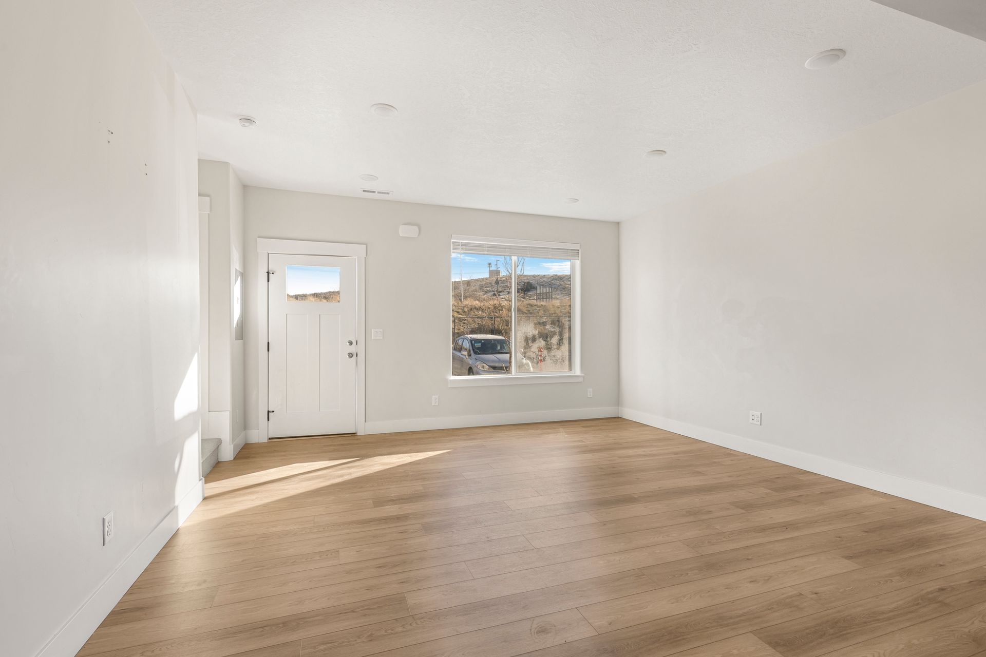Empty room with white walls, wood floors, a door, and a window.
