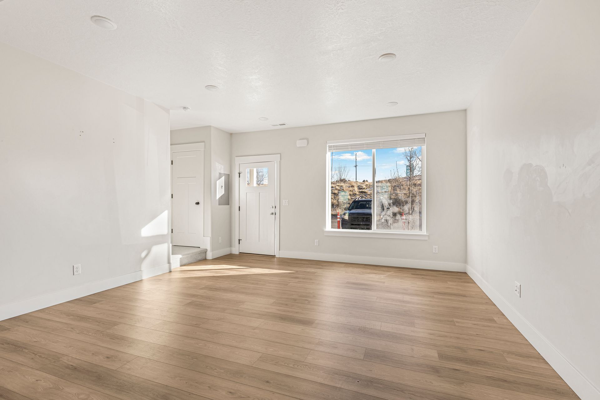 Empty room with hardwood floors, white walls, and a window overlooking a hillside.