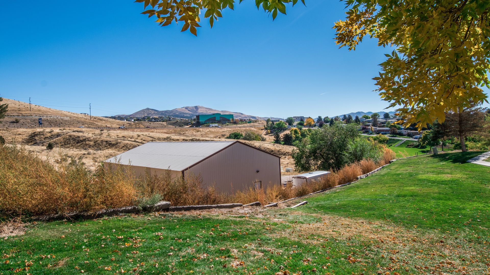 A metal-roofed building on a grassy hill, with dry brush and distant mountains under a blue sky.