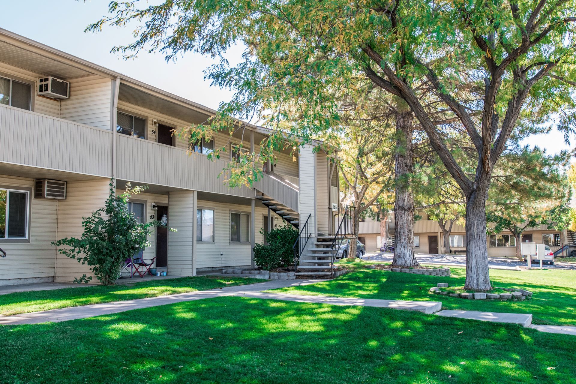 Apartment building with beige exterior, green lawn, and mature trees.
