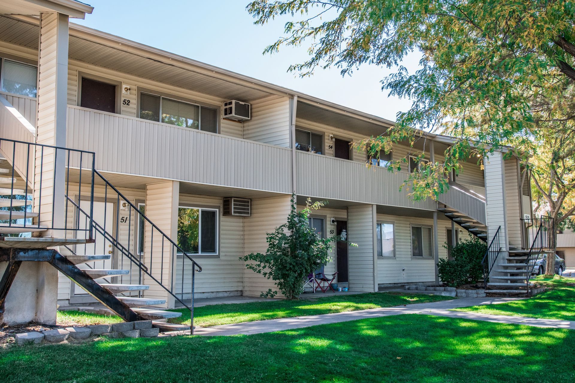 Two-story apartment building with staircases, air conditioning units, and green lawn.