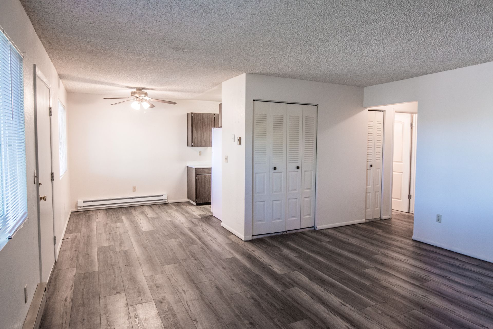 Empty apartment interior with gray flooring, white walls, and a small kitchen visible in the background.