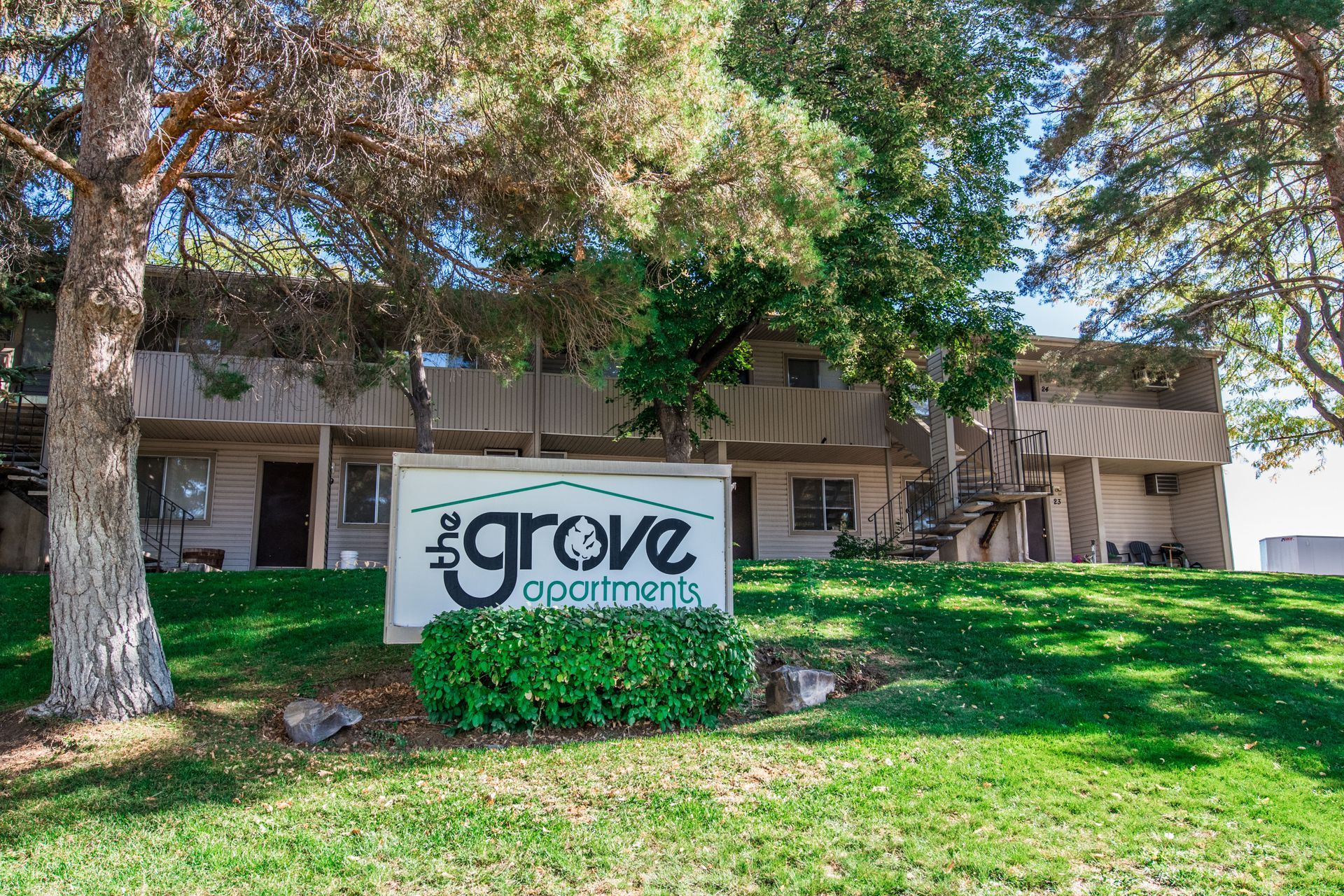 Grove Apartments sign in front of a two-story building on a grassy lawn with trees.