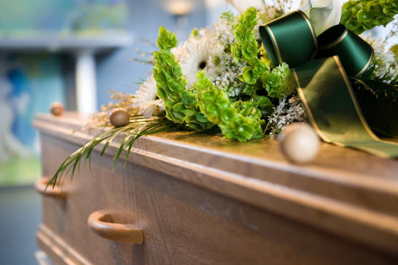 A wooden coffin with flowers and a green bow on it.