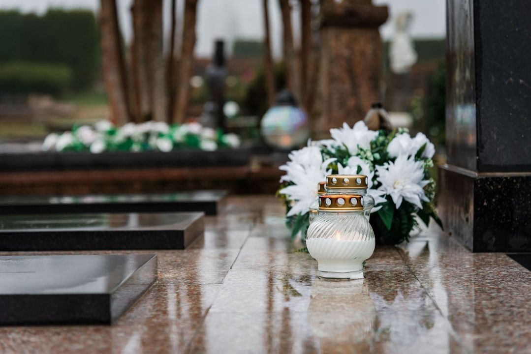 A candle and flowers are on the ground in a cemetery.