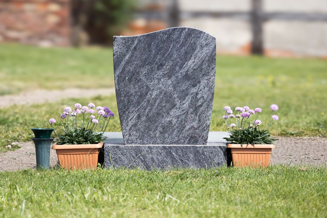 A gravestone in a cemetery with flowers in pots.