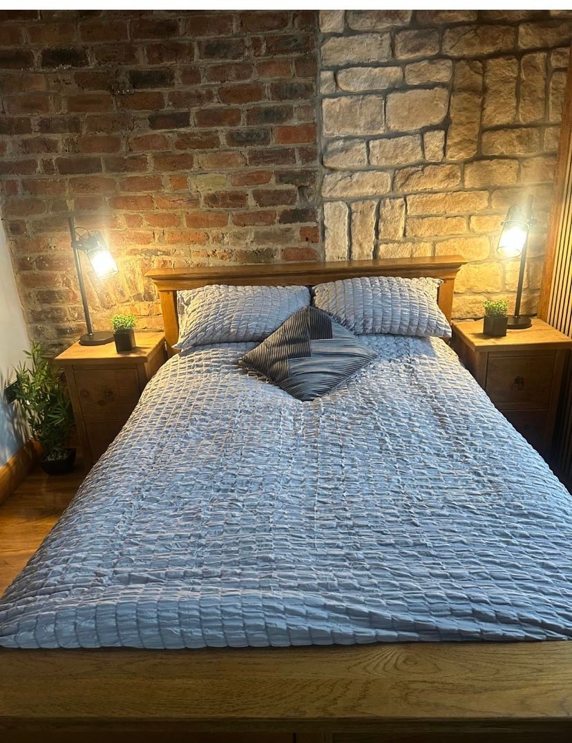 A bedroom with a bed , nightstands , and a brick wall.