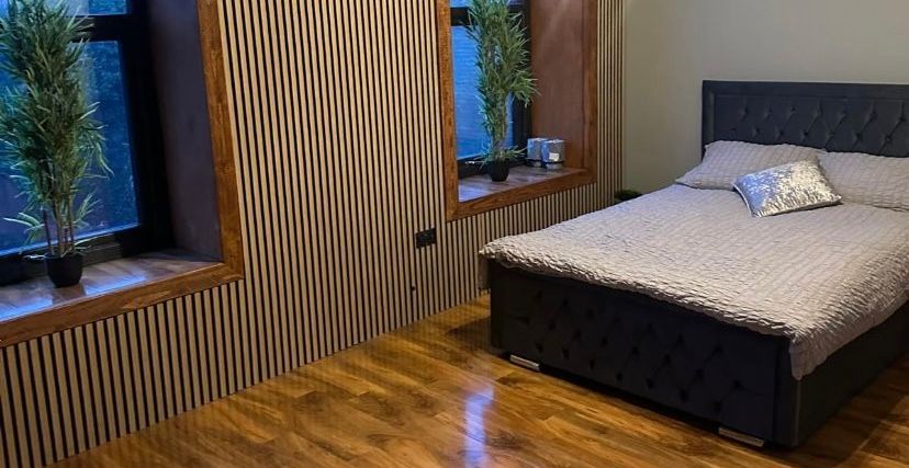 A bedroom with a bed , two windows and a wooden floor.