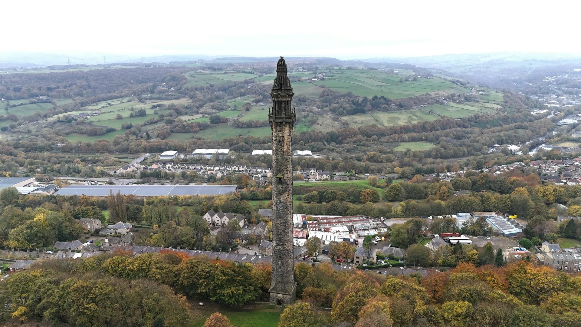 An aerial view of a tower in the middle of a forest with a city in the background.