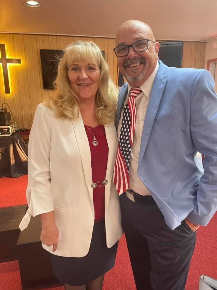 A man and woman standing next to each other in a church. Man has an American flag tie.