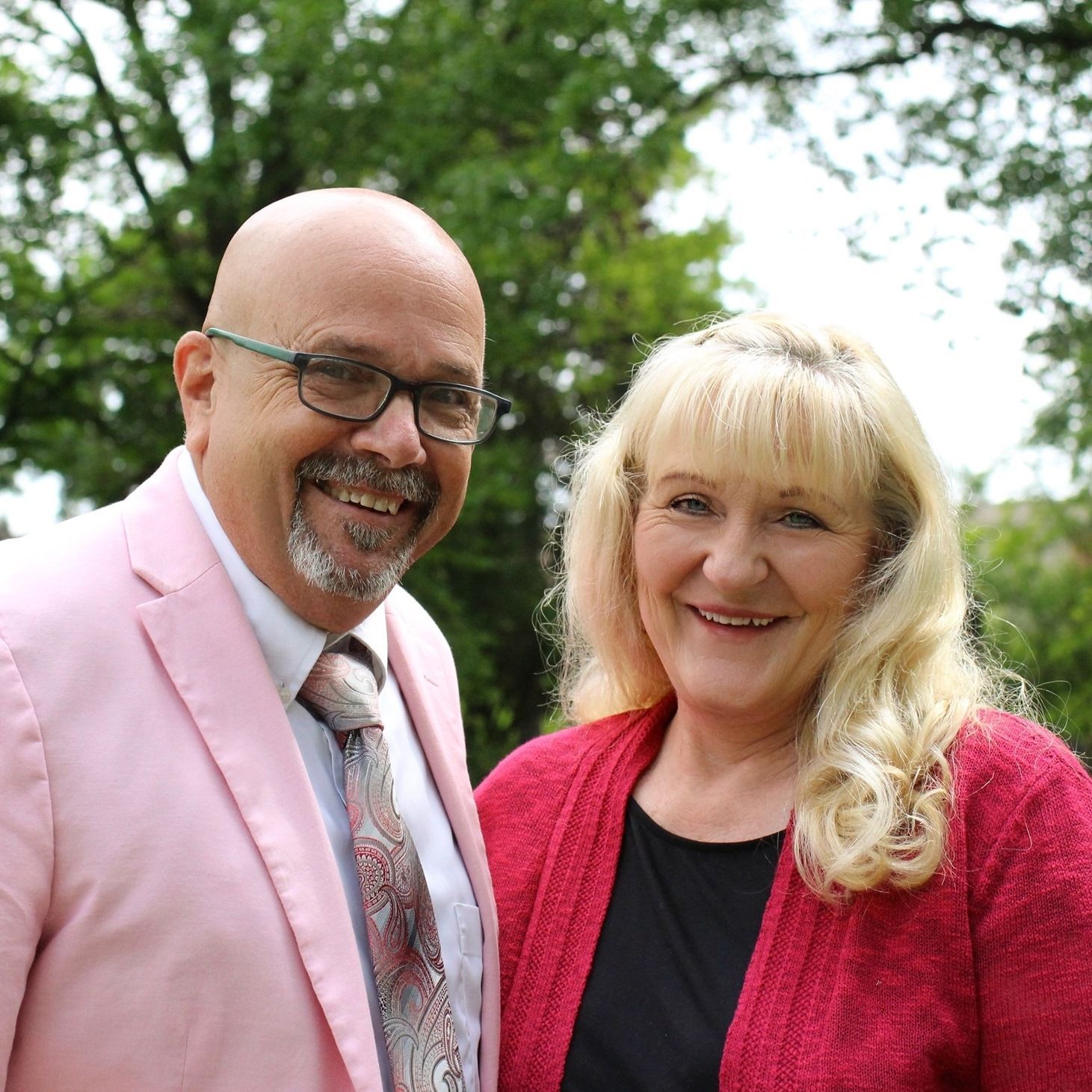 Man in pink suit and woman in red sweater smile outdoors.