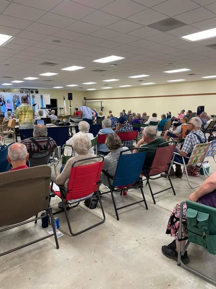 Audience at a meeting, seated in chairs. A speaker is at a table at the front of the room.
