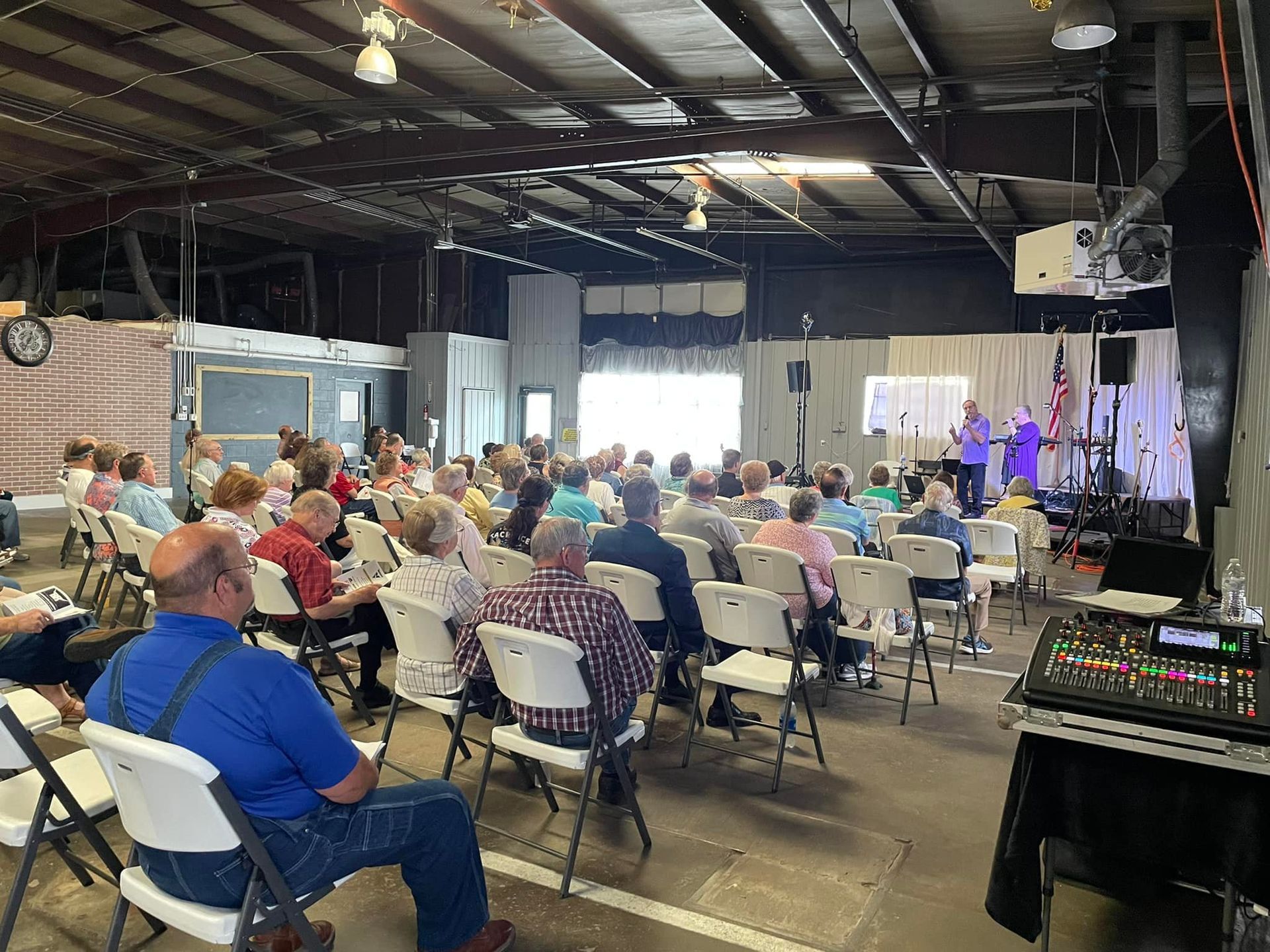 A group of people seated in chairs watching a performance on a stage indoors, in a large, open room.