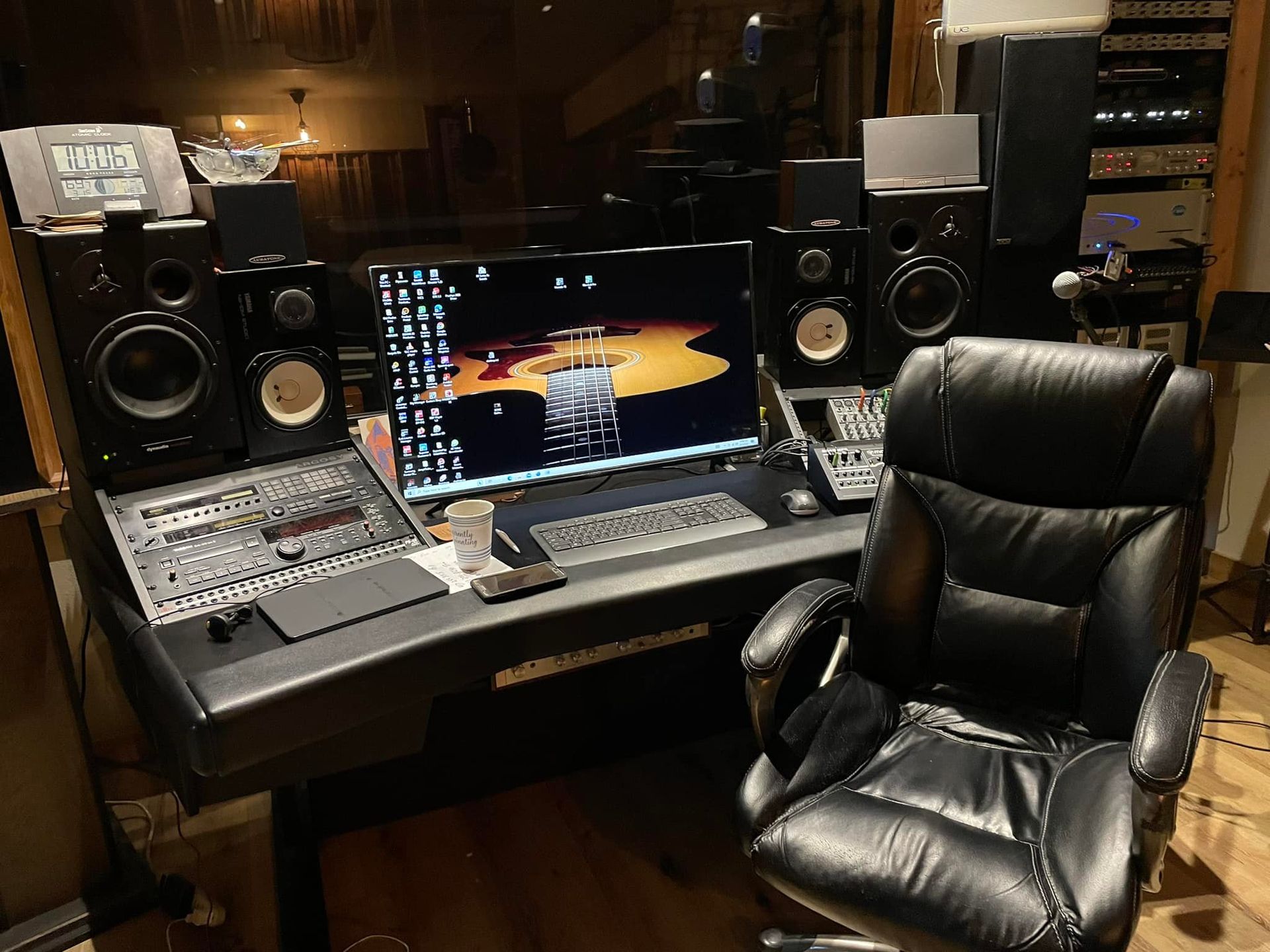 Recording studio desk with computer, speakers, mixing console, and black leather chair.