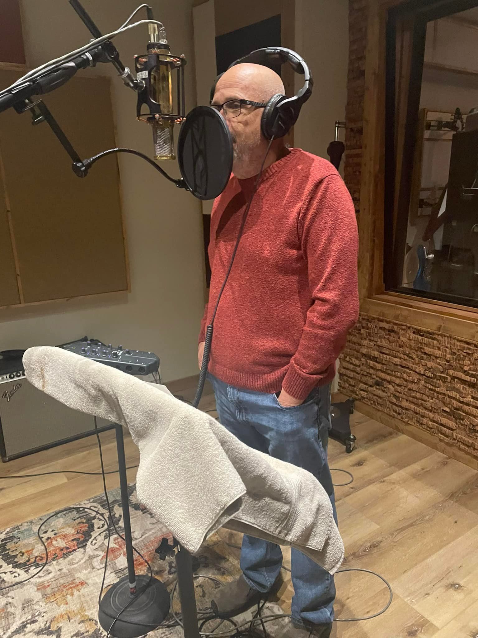 Man in red shirt singing into a microphone in a recording studio.