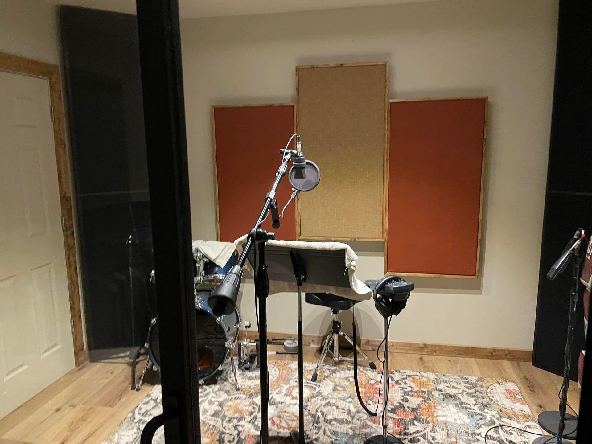 Recording studio with drum set, microphones, acoustic panels, and a rug.
