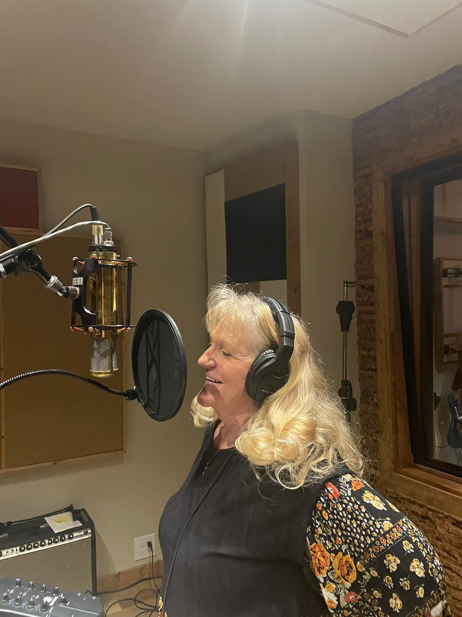 Woman singing into a microphone in a recording studio, wearing headphones and a black top.