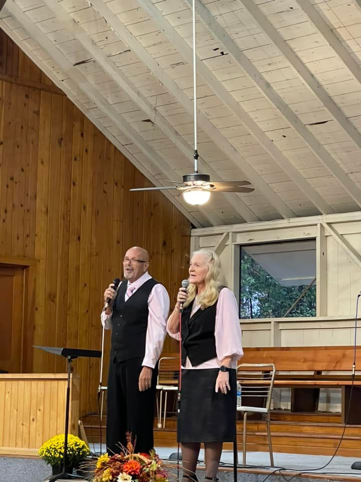 Two people, a man and woman, singing into microphones in a church.