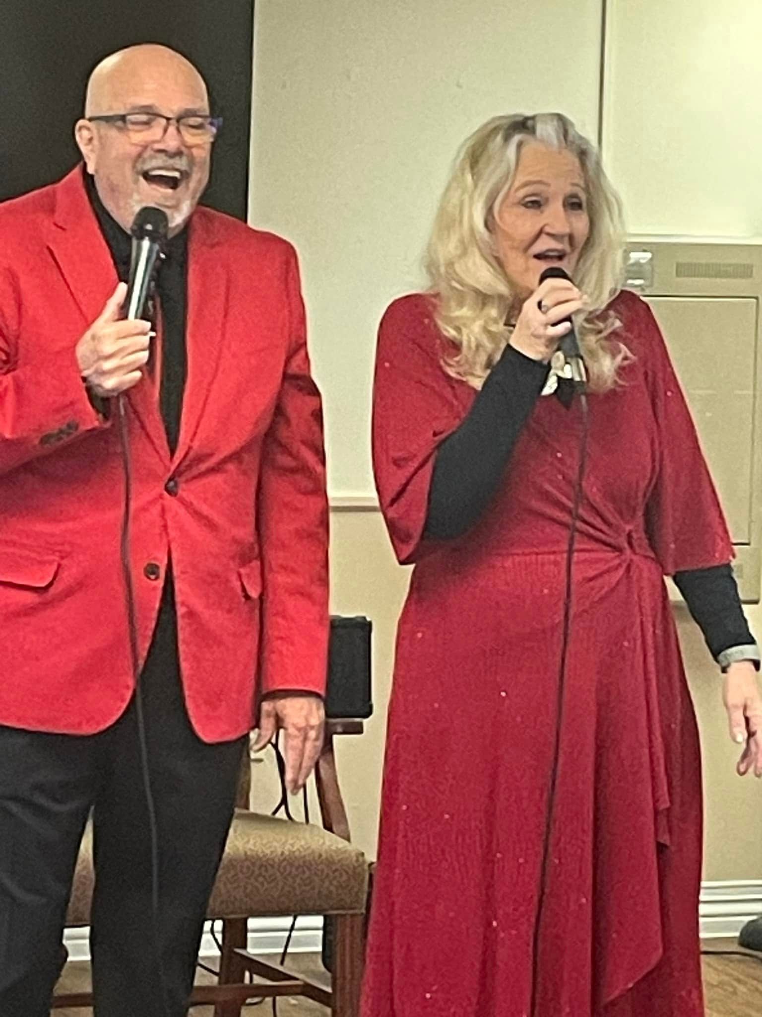 Man in red suit and woman in red dress singing into microphones.